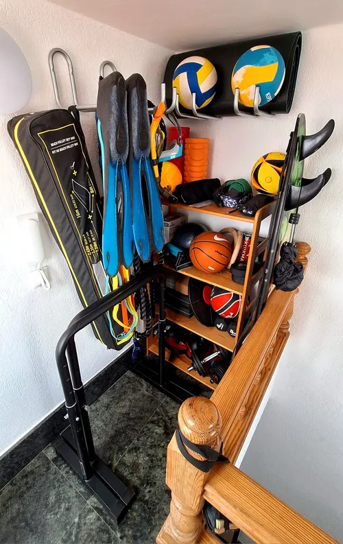 The sport equipment corner on the U32 staircase landing: wall rack with volleyballs and swim fins, a wooden shelf with balls, weights and gymnastic rings, a free-standing bar frame